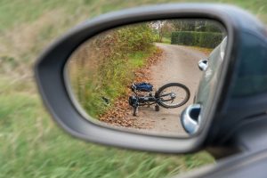 A fallen bicycle lies on a rural road, seen through the side mirror of a parked car.