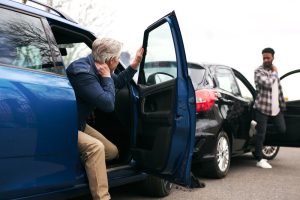 Two men exit their vehicles after a car accident; a blue SUV and a black car are shown with visible damage.