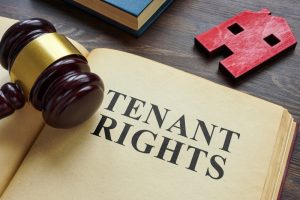 A gavel rests on an open book displaying the words "Tenant Rights," with a small red house cutout nearby on a wooden table.