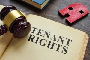 A gavel rests on an open book displaying the words "Tenant Rights," with a small red house cutout nearby on a wooden table.