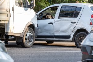A white van and a white car involved in a side-impact collision on a road, with visible damage to the car’s driver-side door.